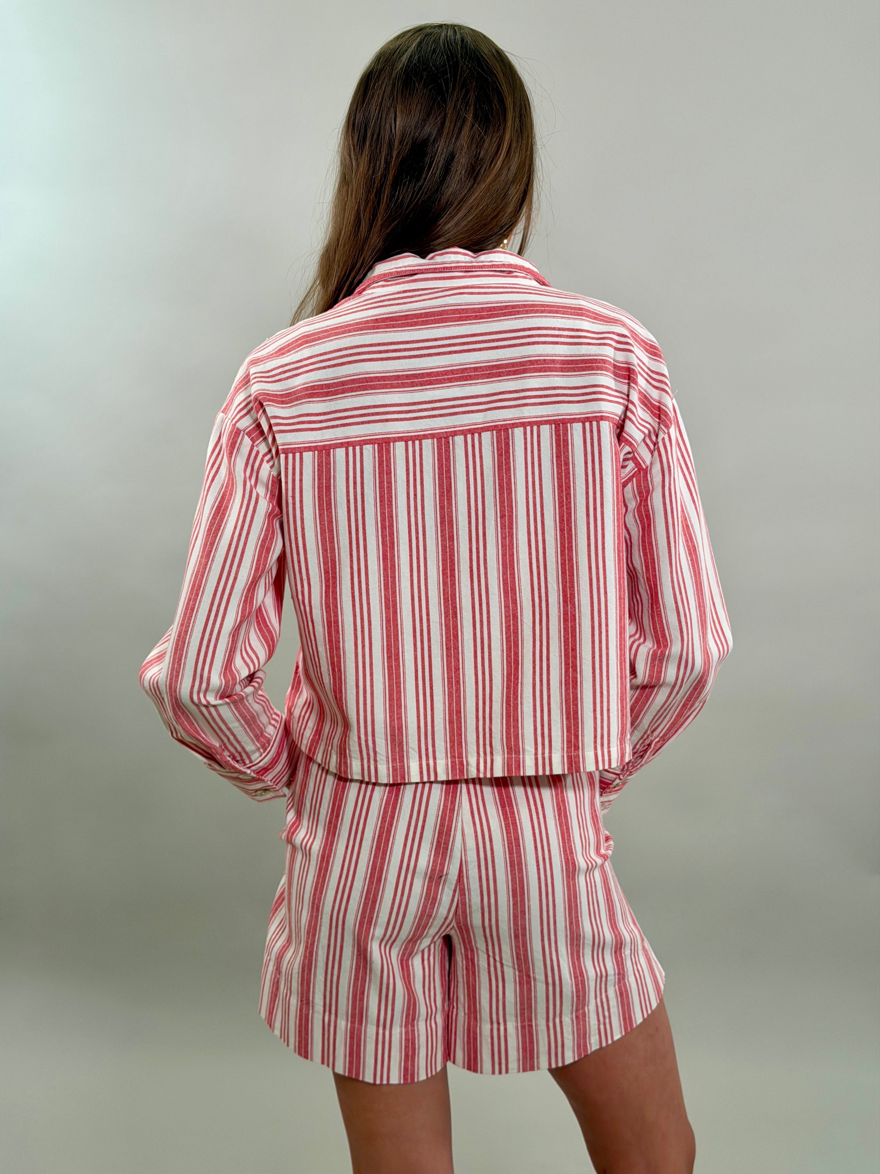 The back of a woman wearing tailored red and white striped shorts and a matching cropped long-sleeve button-down shirt.