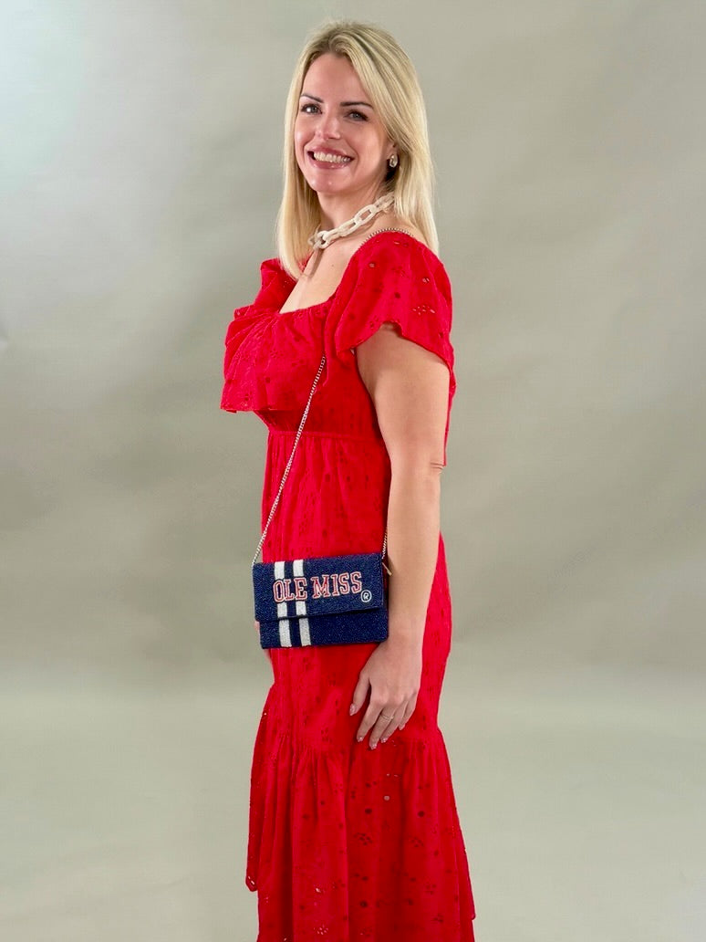 Close up of a side view woman in a red eyelet dress holding a blue and white bag with &