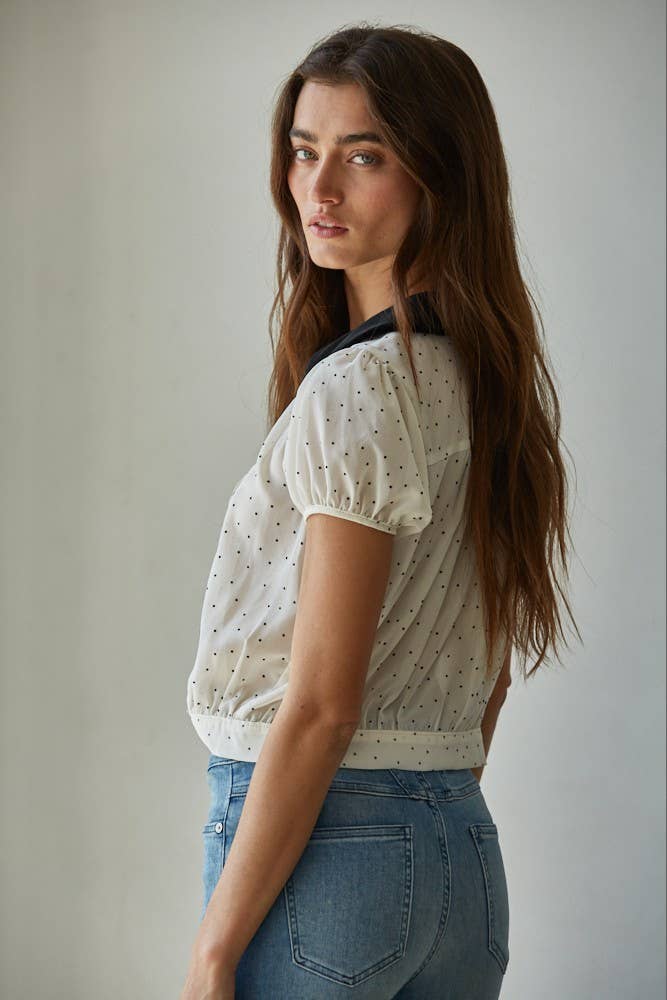 Woman wearing the black and white polka dot blouse with a velvet Peter Pan collar and a blue jean against a white background.