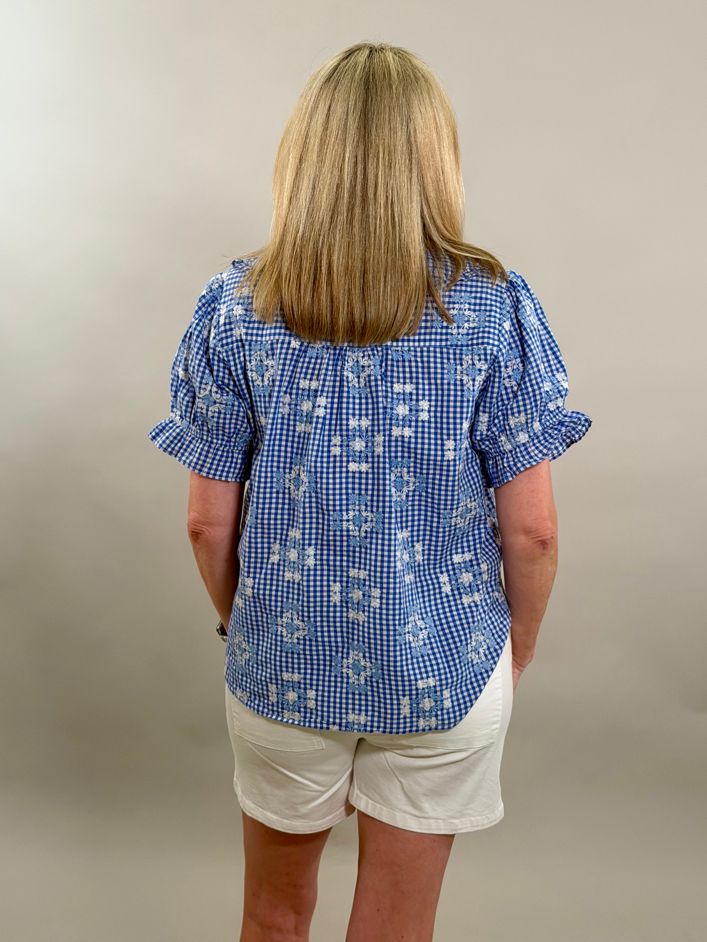 Person wearing a blue checkered shirt and white shorts against a plain background