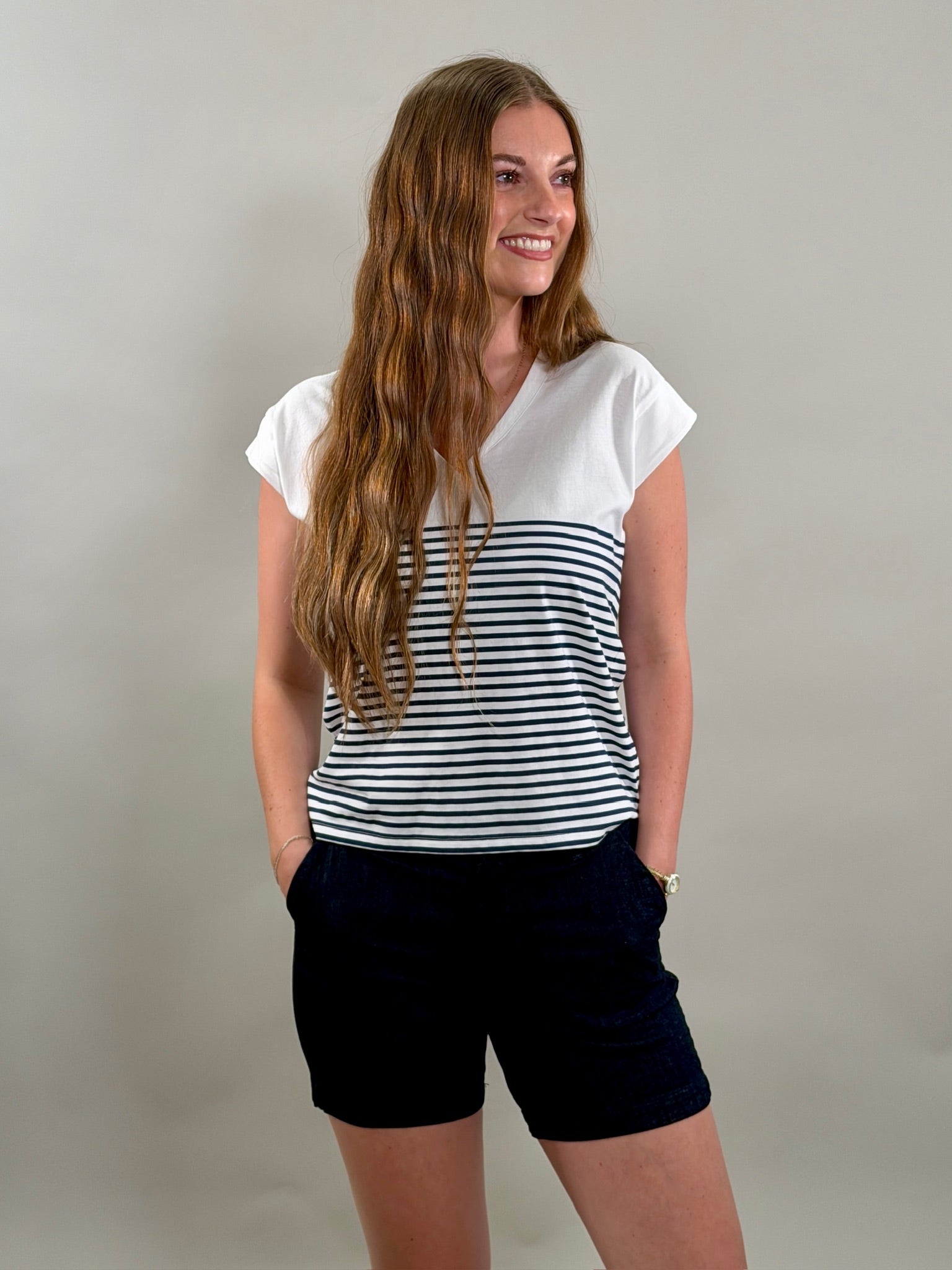 Smiling woman wearing a white t-shirt with navy stripes and navy shorts on a plain background.