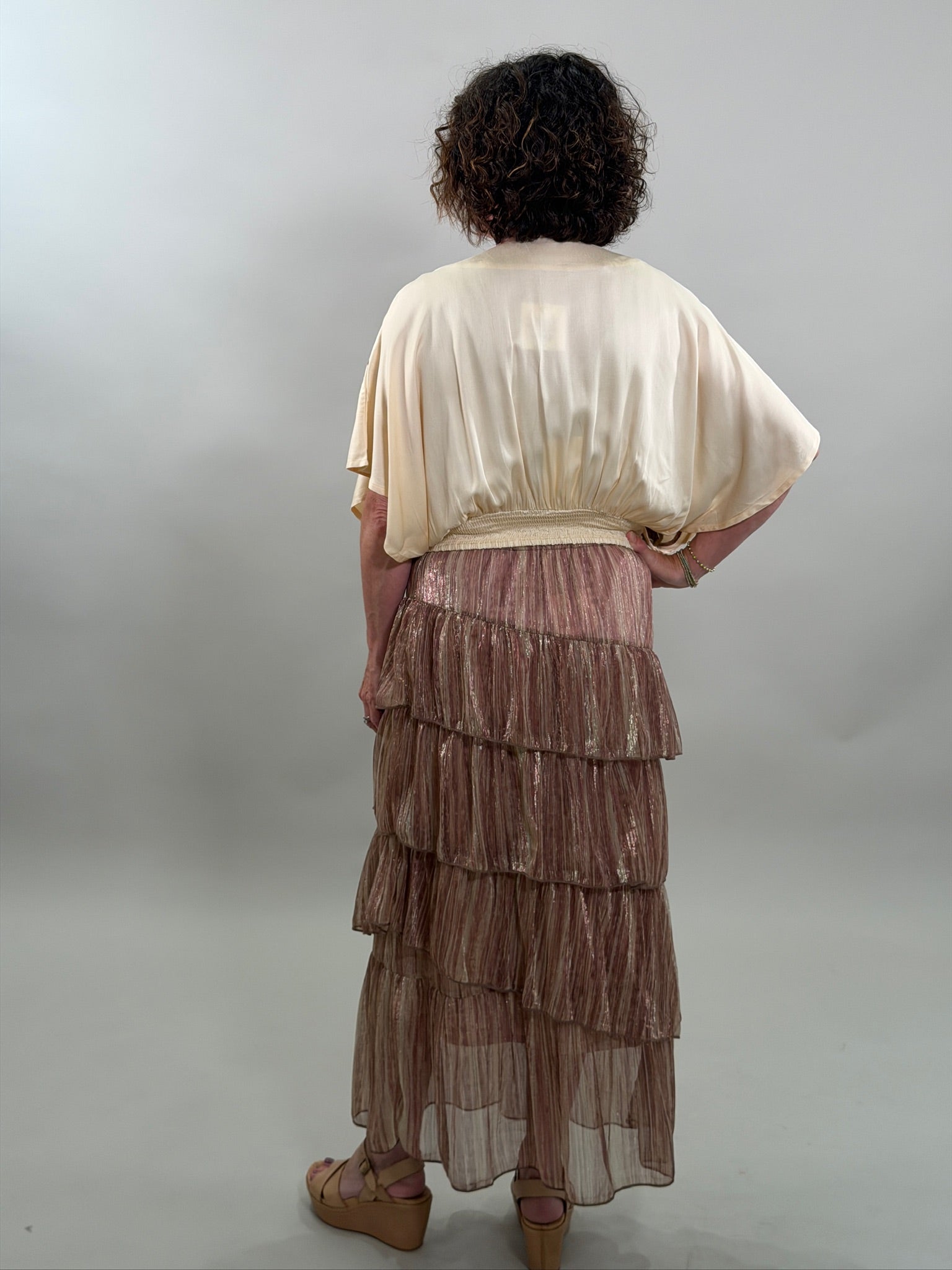 Rear view of a woman wearing a cream-colored bohemian blouse and a ruffled skirt with a smocked waist.