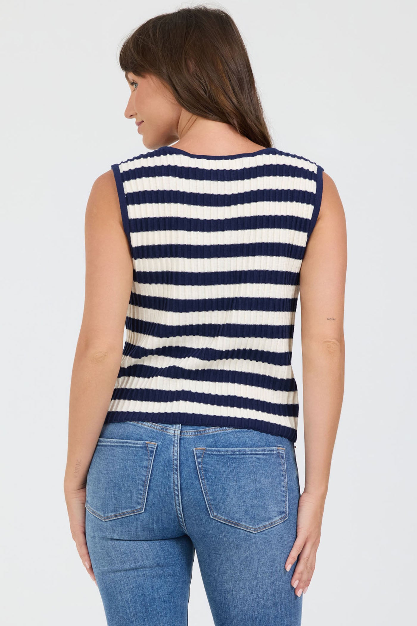 Rear view of a woman wearing a navy and white striped sleeveless sweater with blue jeans on a light gray background