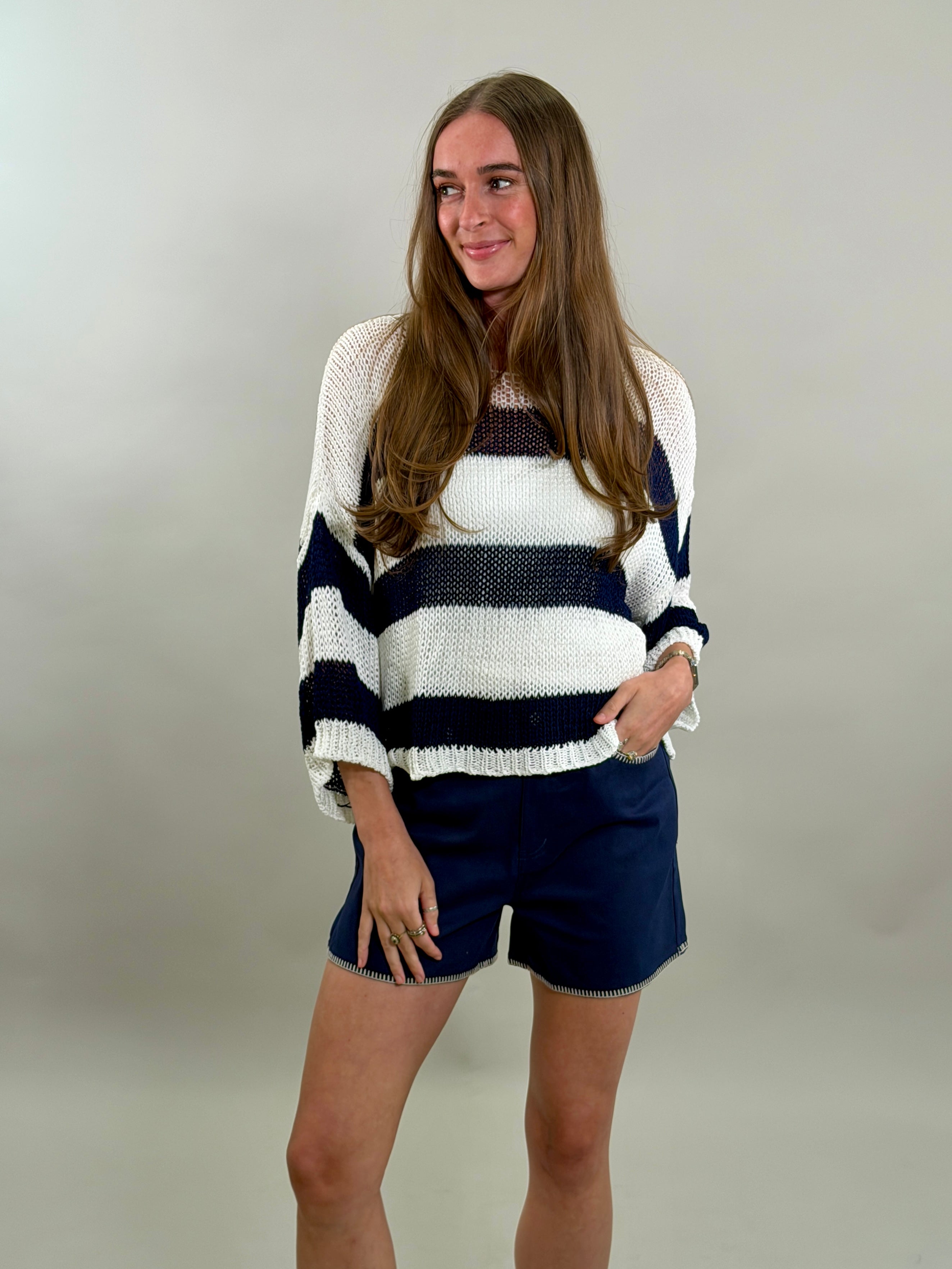 Woman looking to the side wearing a striped sweater and shorts against a plain background