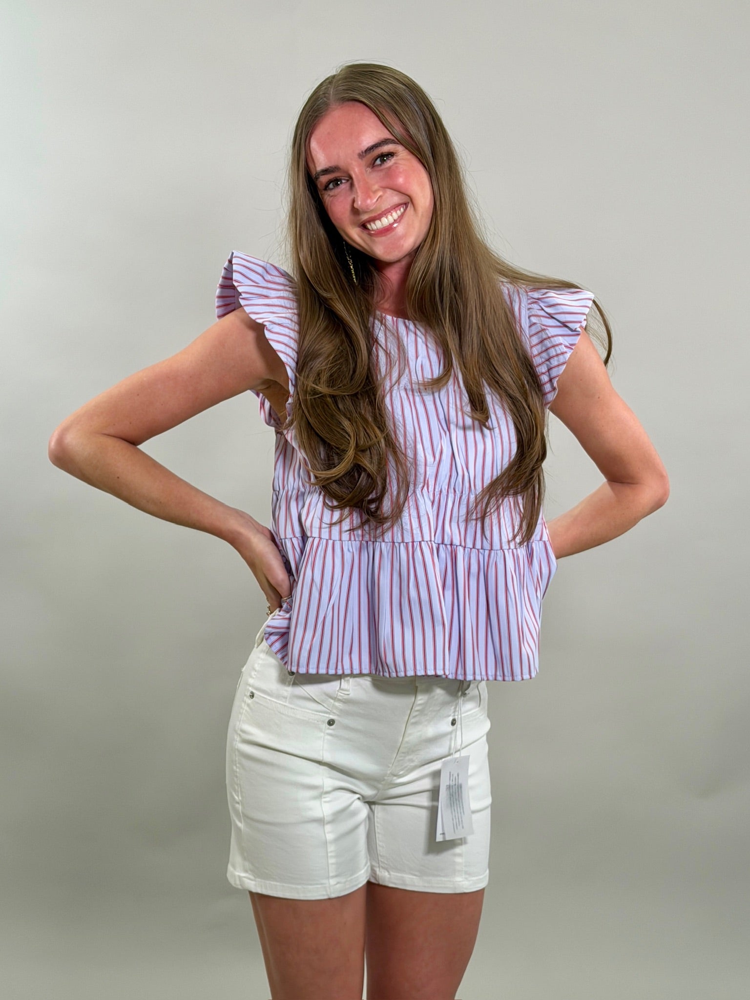 A smiling woman wearing a blue, red, and white striped top and white shorts against a plain background