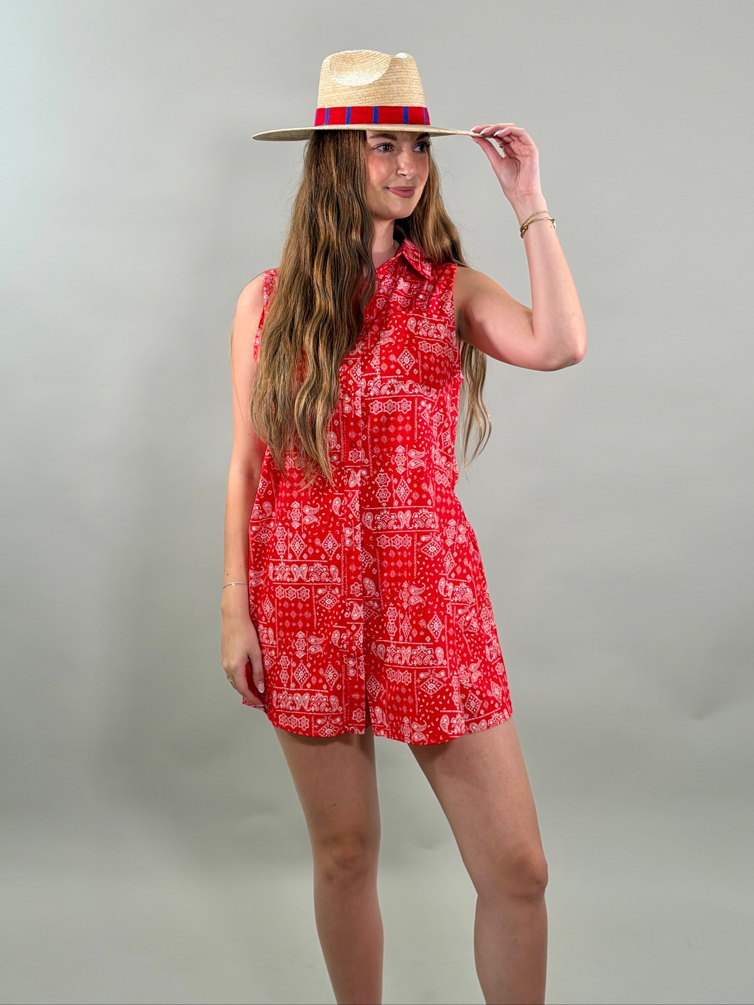 Woman wearing a red patterned romper and straw hat on a gray background