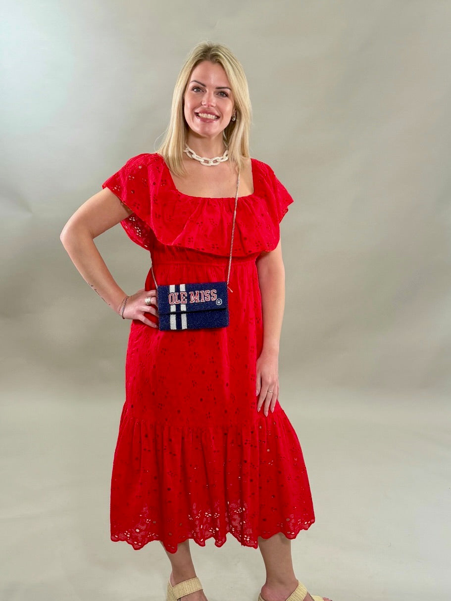 Woman wearing a red dress with a beaded Ole Miss handbag against a plain background.