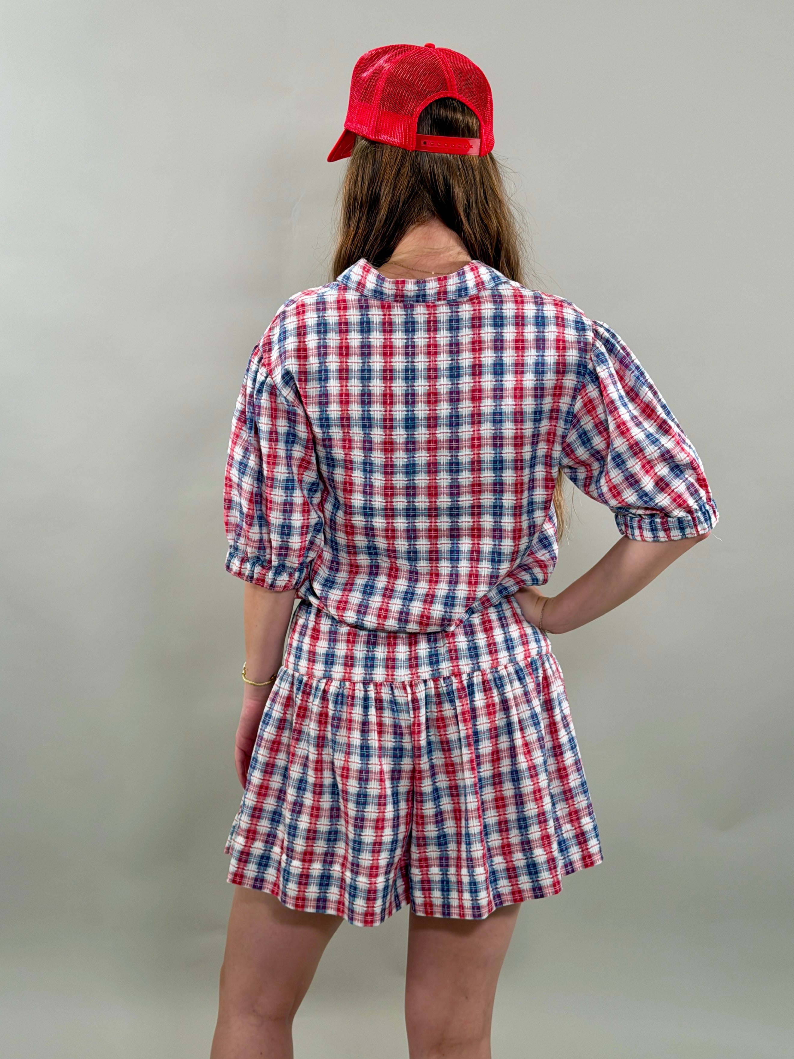 Person wearing a red, white, and blue checkered outfit with a red cap on a plain background