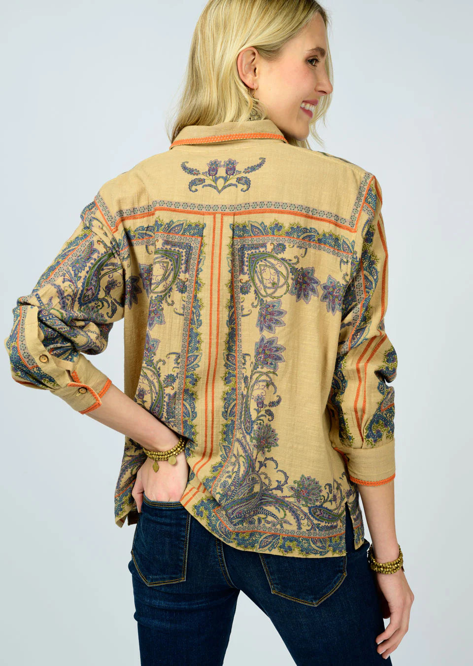 Woman wearing a patterned beige shirt with long sleeves on a plain background