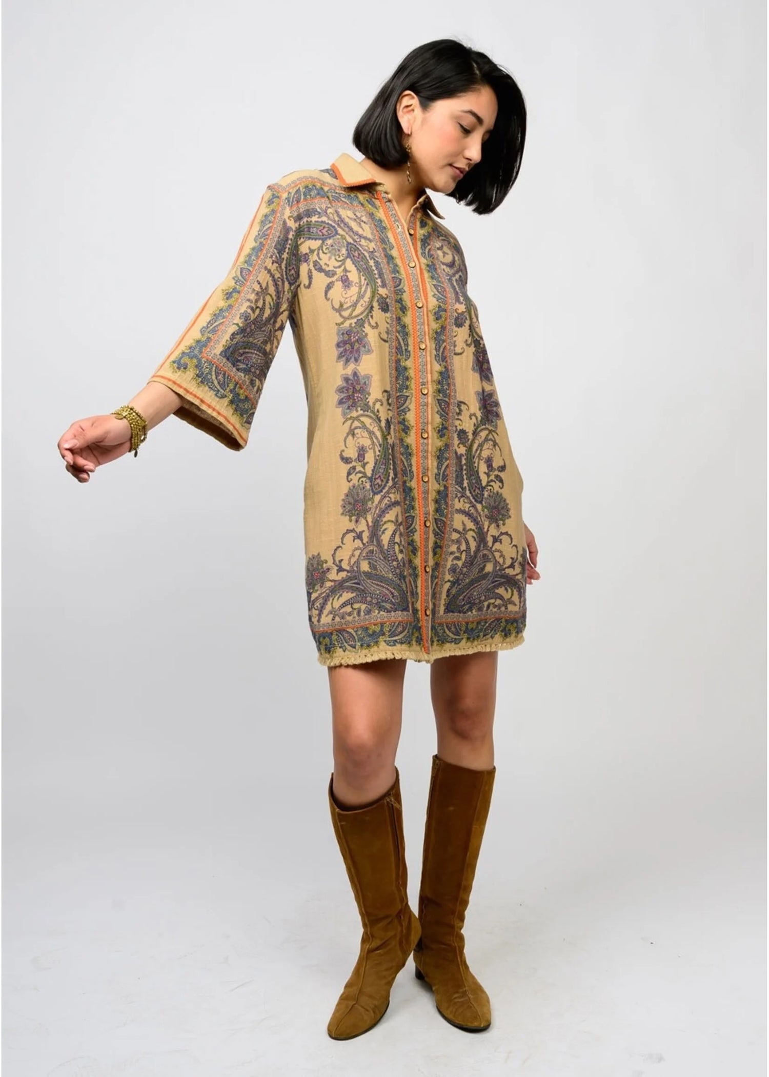 Woman wearing a patterned dress with bell sleeves and brown boots on a white background