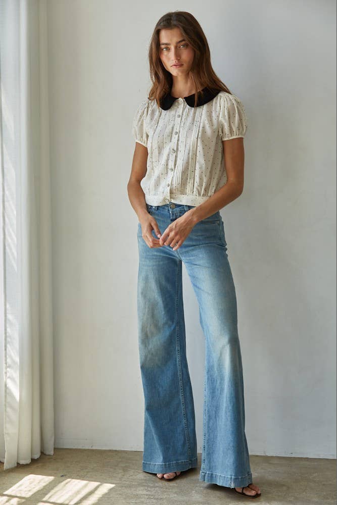 Woman wearing the black and white polka dot blouse with a velvet Peter Pan collar and a blue jean against a white background.