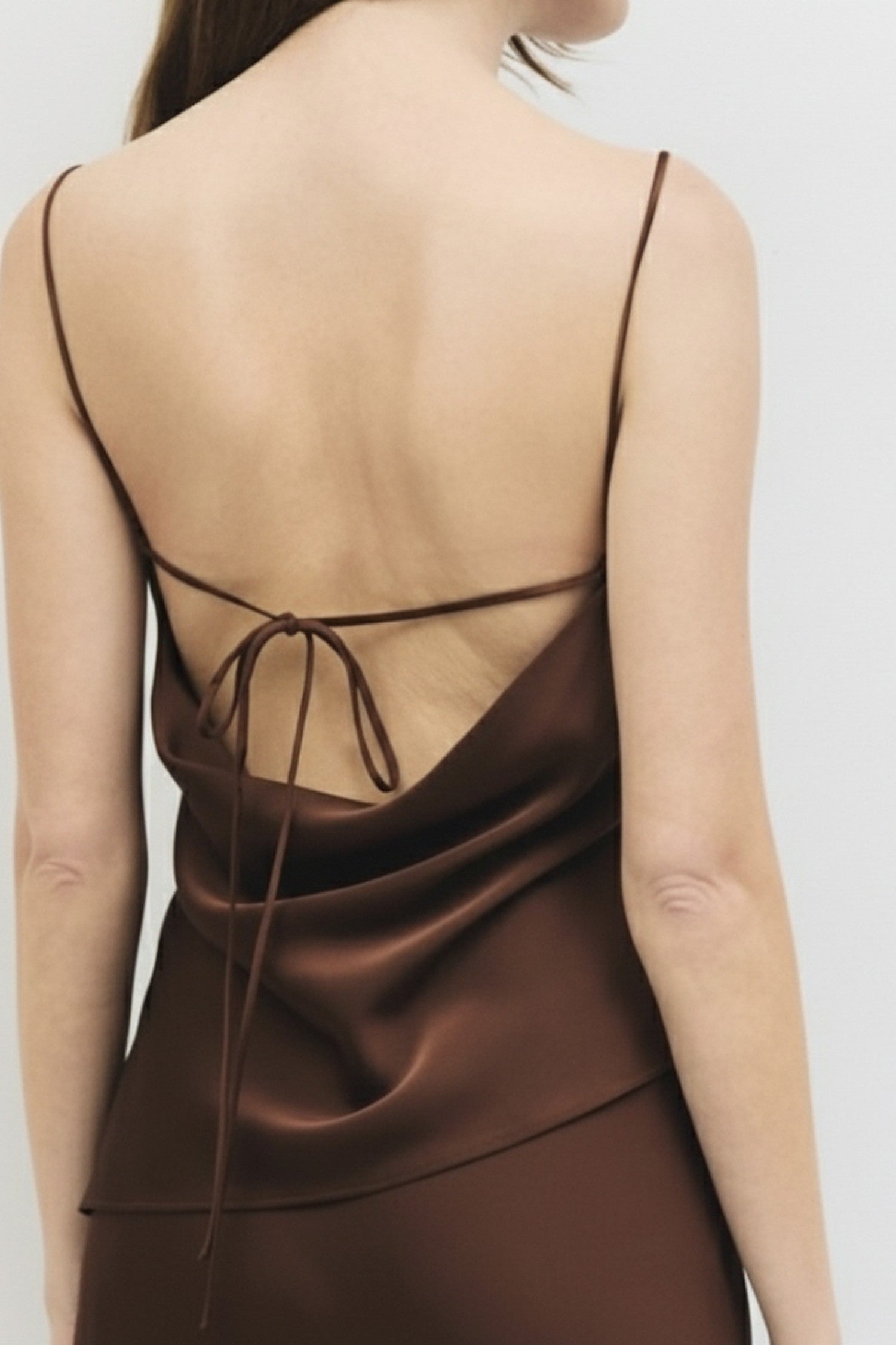 Close up rear view of a woman wearing a chocolate brown satin cowl neck tank.