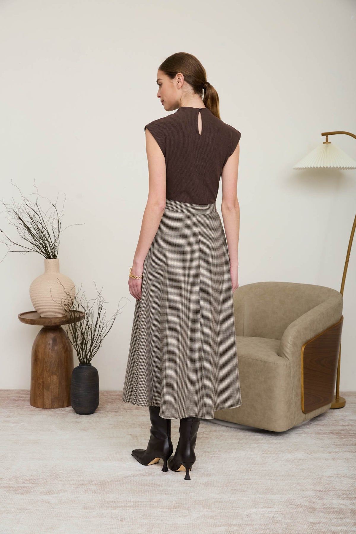 Rear view of a woman wearing a sophisticated midi dress featuring a chocolate brown ribbed knit mock-neck top and a neutral houndstooth A-line skirt with a matching tie belt.