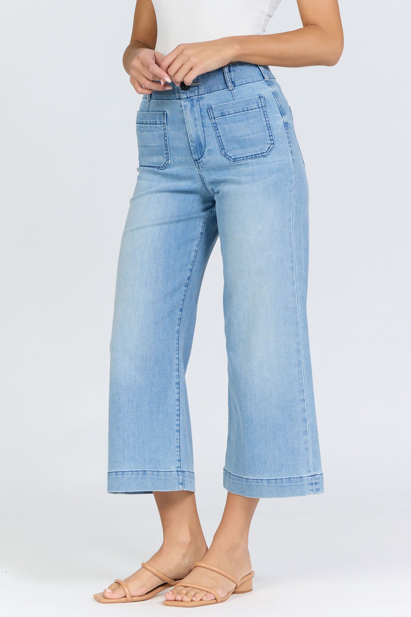 Side view of a woman wearing light-wash high-rise wide-leg cropped jeans with front patch pockets and tan slide sandals.