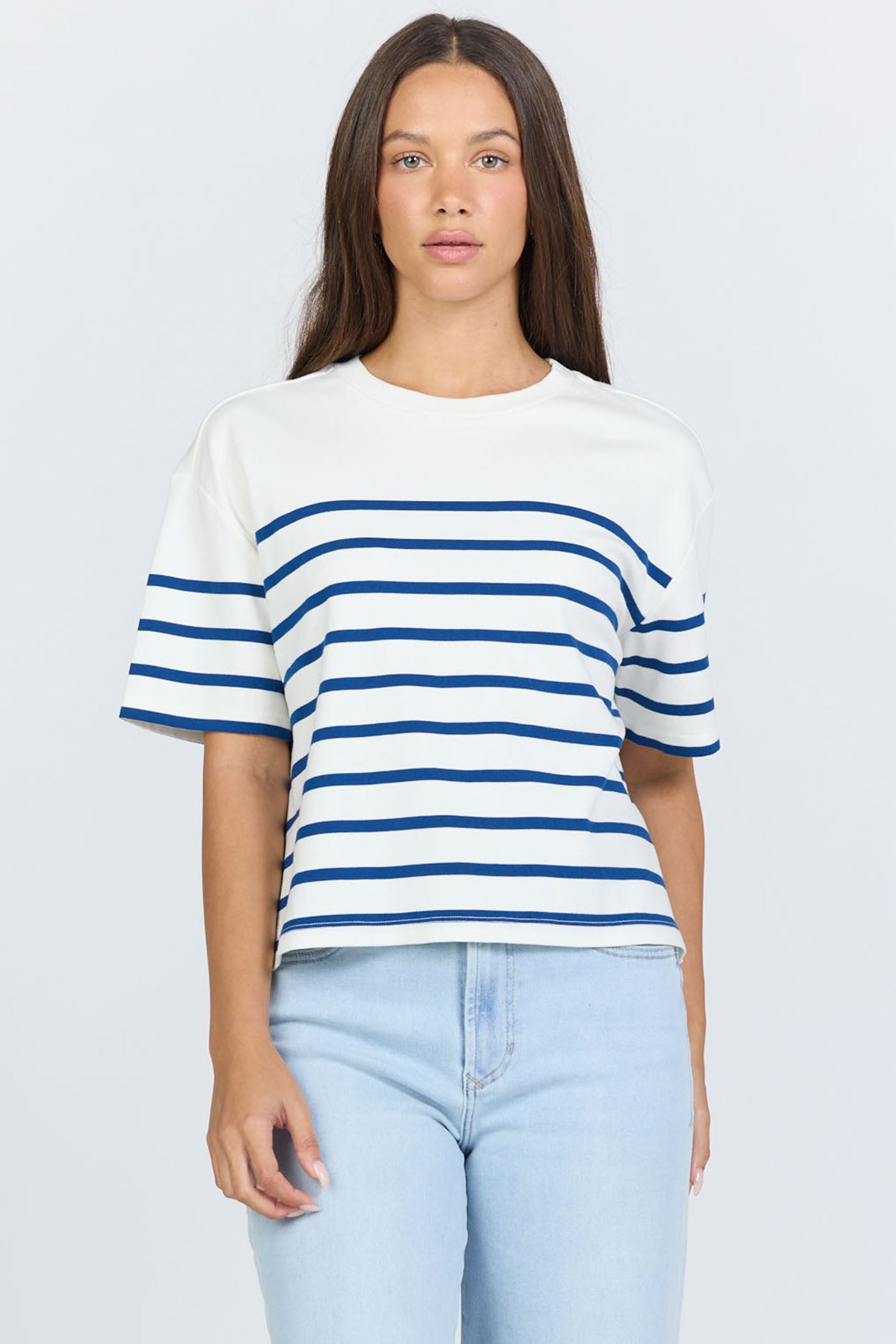 Front view of a woman wearing a white and blue horizontal striped crew neck cotton t-shirt with light-wash jeans.