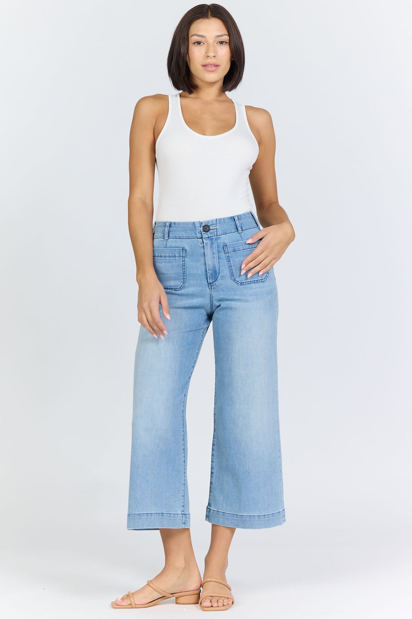 Full body view of a woman wearing light-wash high-rise wide-leg cropped jeans with front patch pockets and tan slide sandals.