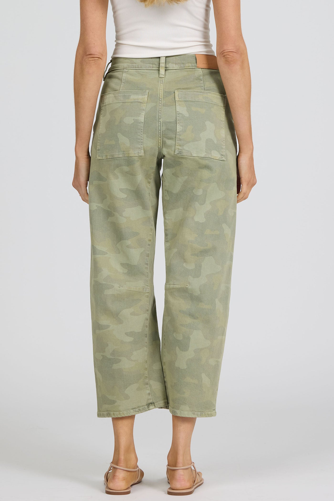 Rear view of a woman wearing green camouflage pants on a white background.