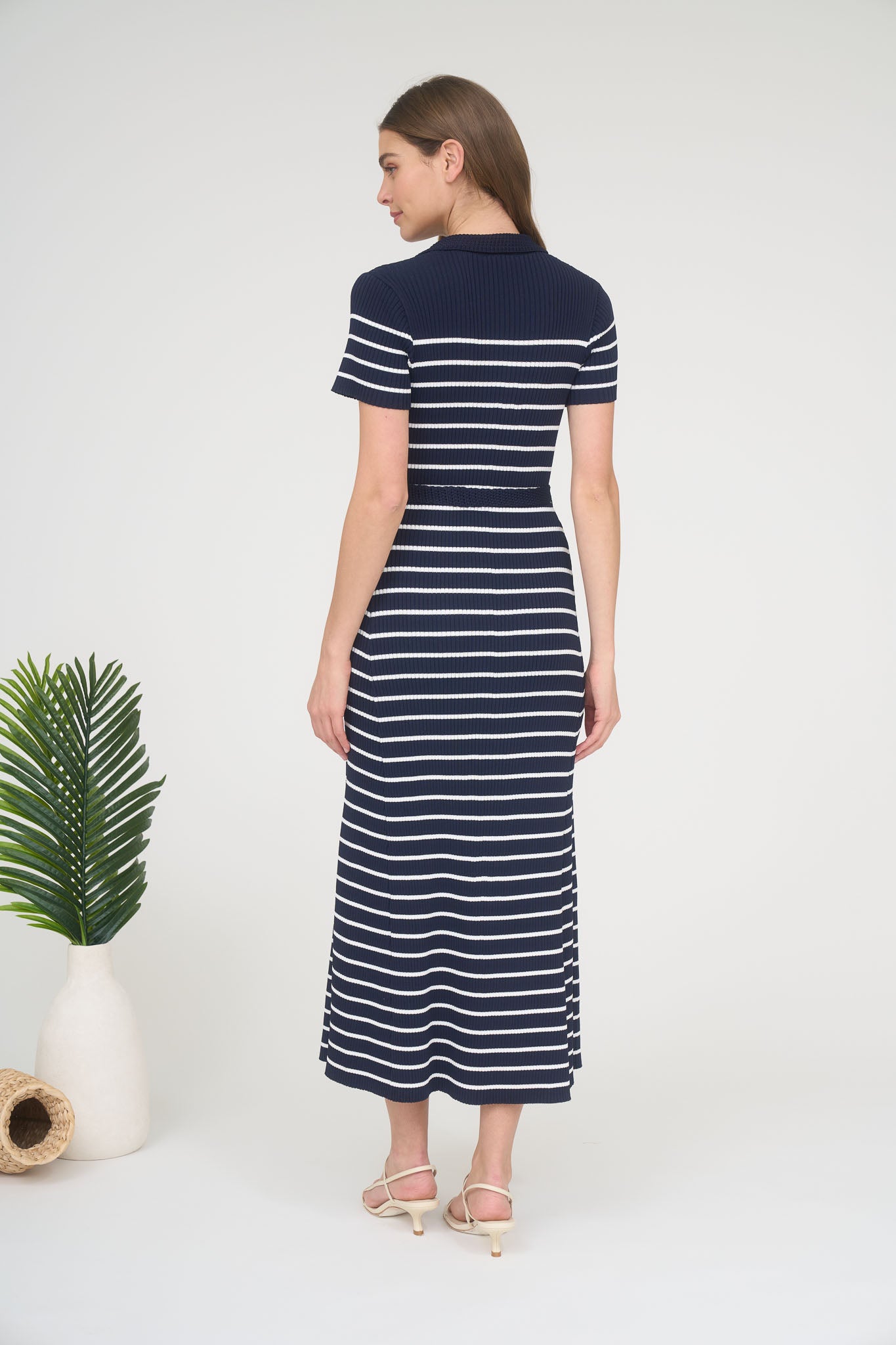 Rear view of a woman wearing a short-sleeve navy and white horizontally striped ribbed knit maxi dress with a matching tie belt.
