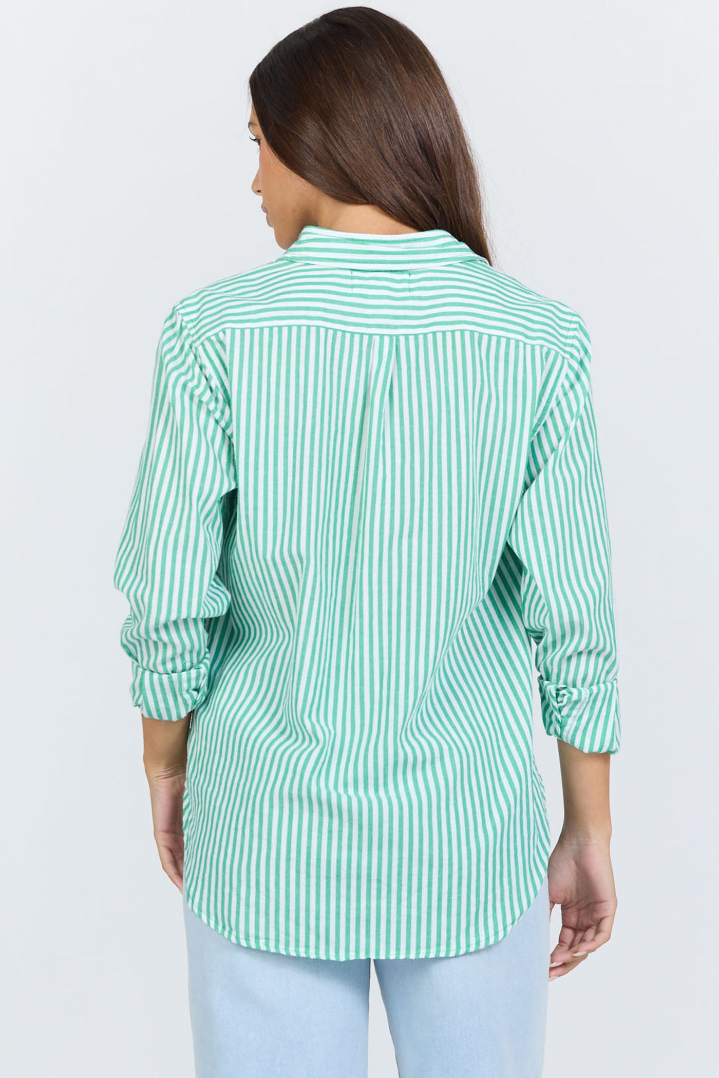 Rear view of a woman wearing a green and white vertical striped long-sleeve cotton button-up shirt with light blue jeans.