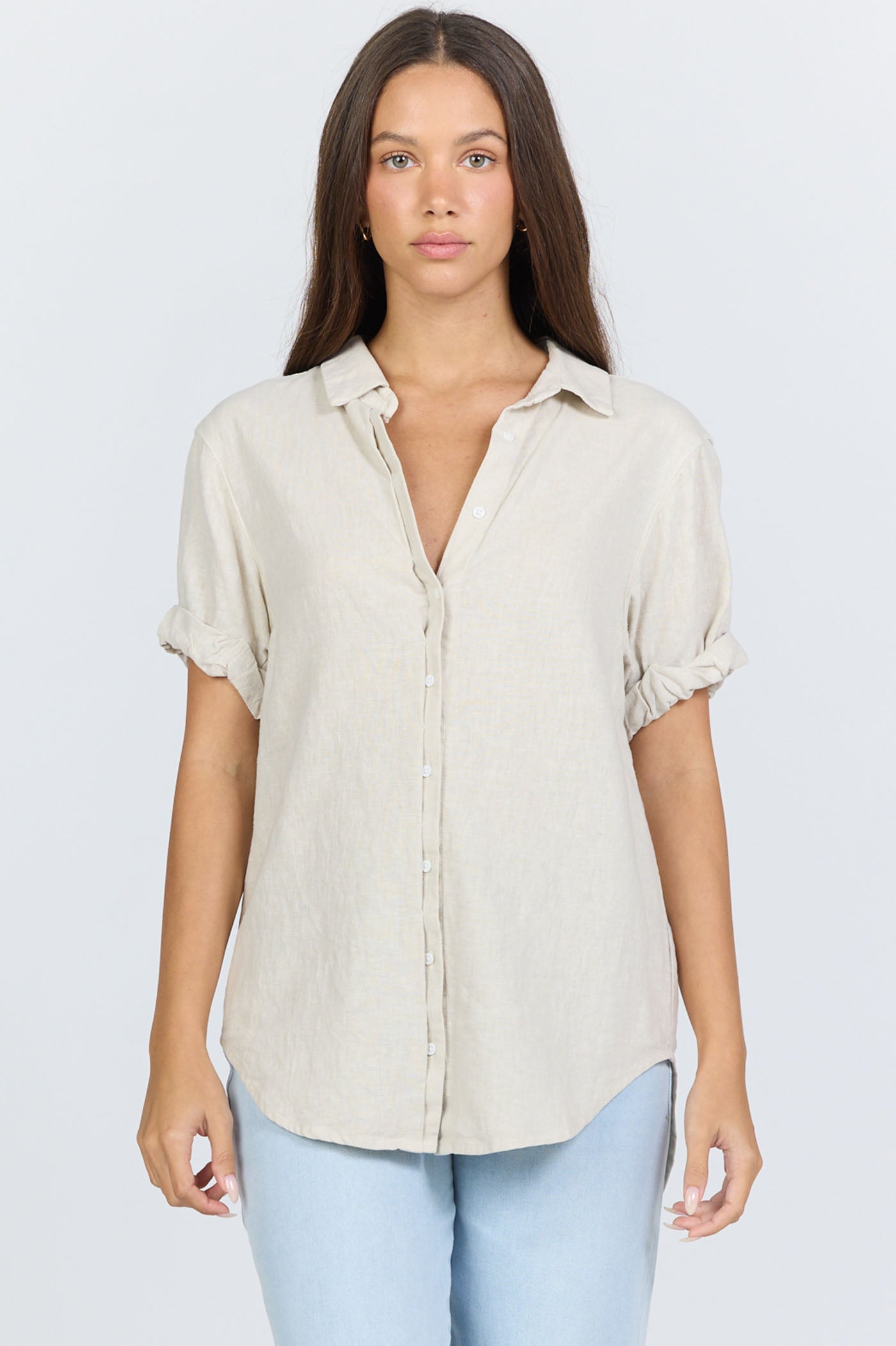Front view of a model wearing a neutral cream linen-blend short sleeve button-down shirt with light blue jeans.