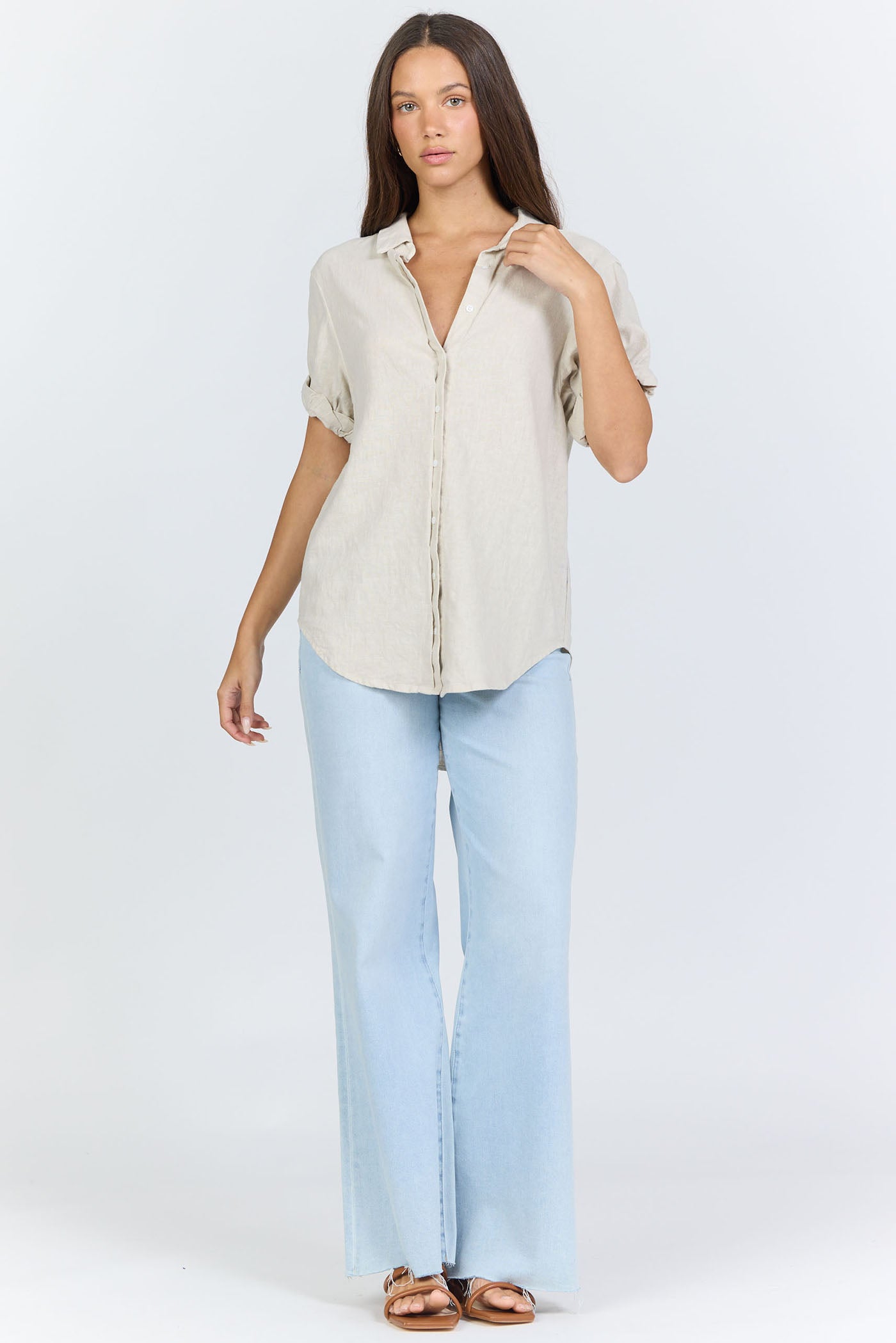 Full body view of a model wearing a neutral cream linen-blend short sleeve button-down shirt with light blue jeans.