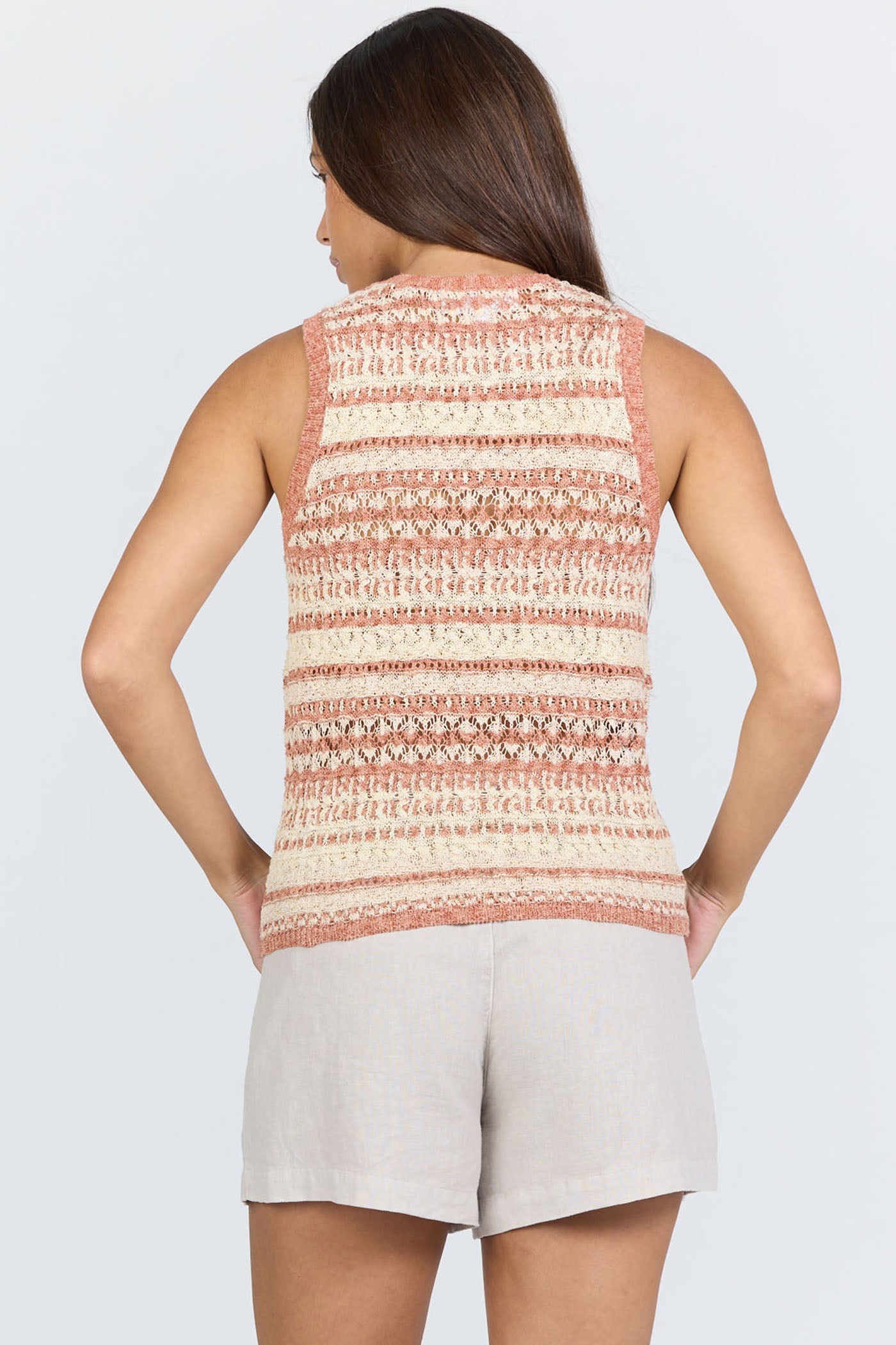 Rear view of a woman wearing a sleeveless crew-neck sweater tank with terra-cotta and ivory horizontal stripes, paired with light linen shorts.