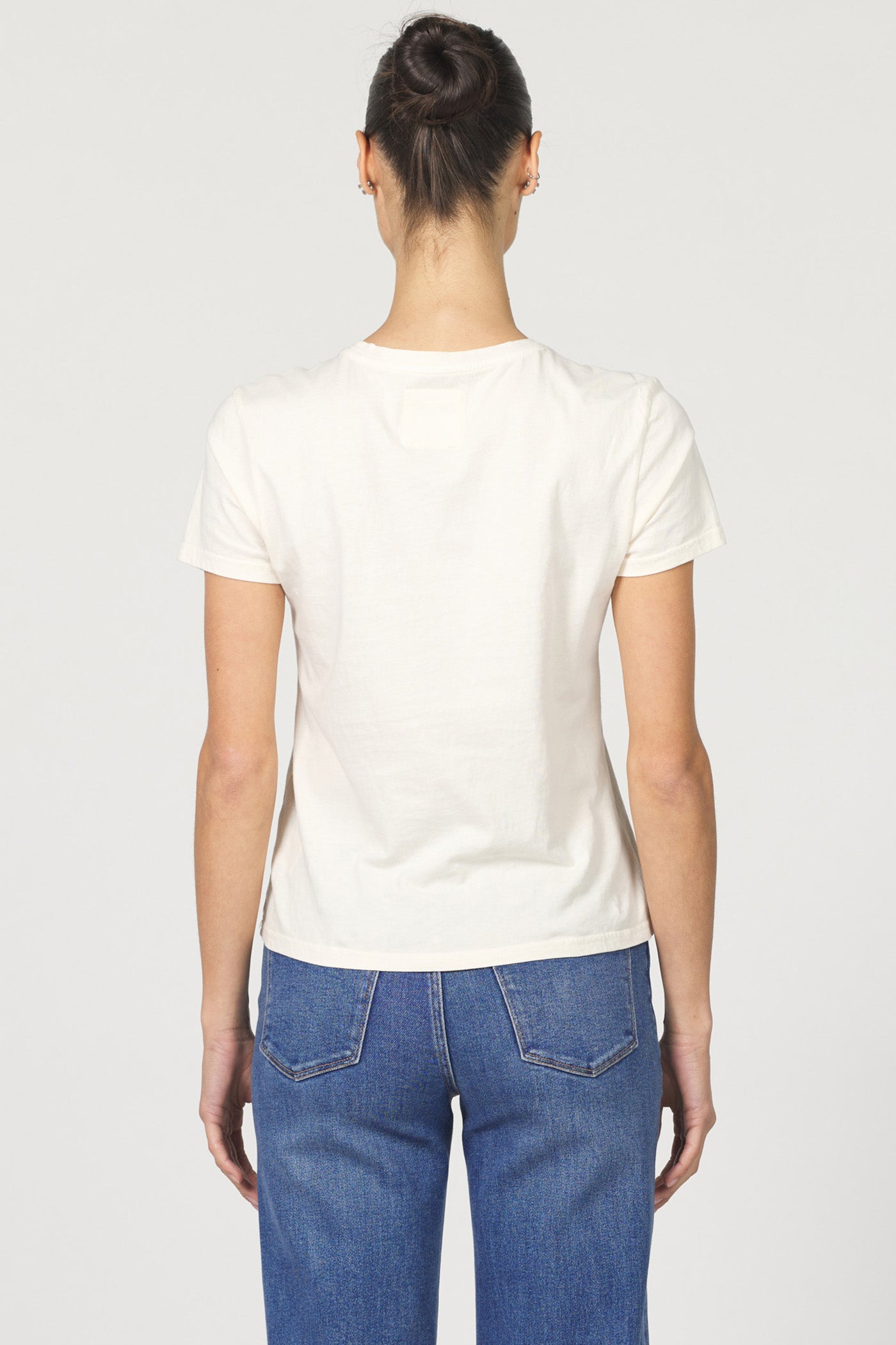 Rear view of a woman wearing a white classic short-sleeve crew neck cotton jersey t-shirt paired with denim