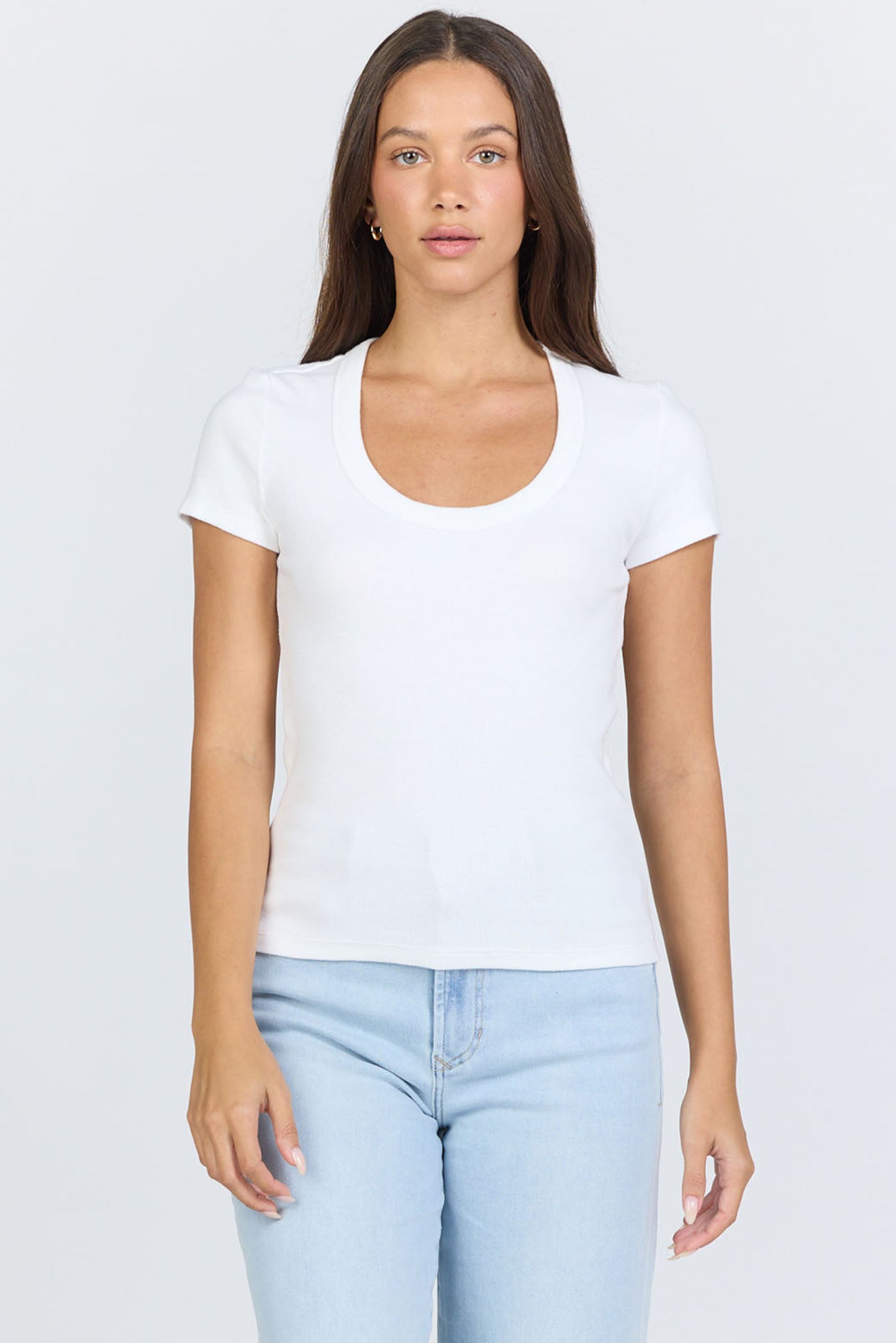 A woman wearing a fitted white scoop-neck short-sleeve t-shirt tucked into blue jeans.