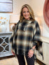 Woman wearing a black, taupe, and mocha plaid poncho with a cowl neck and fringe trim.