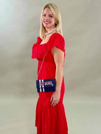 Close up of a side view woman in a red eyelet dress holding a blue and white bag with &