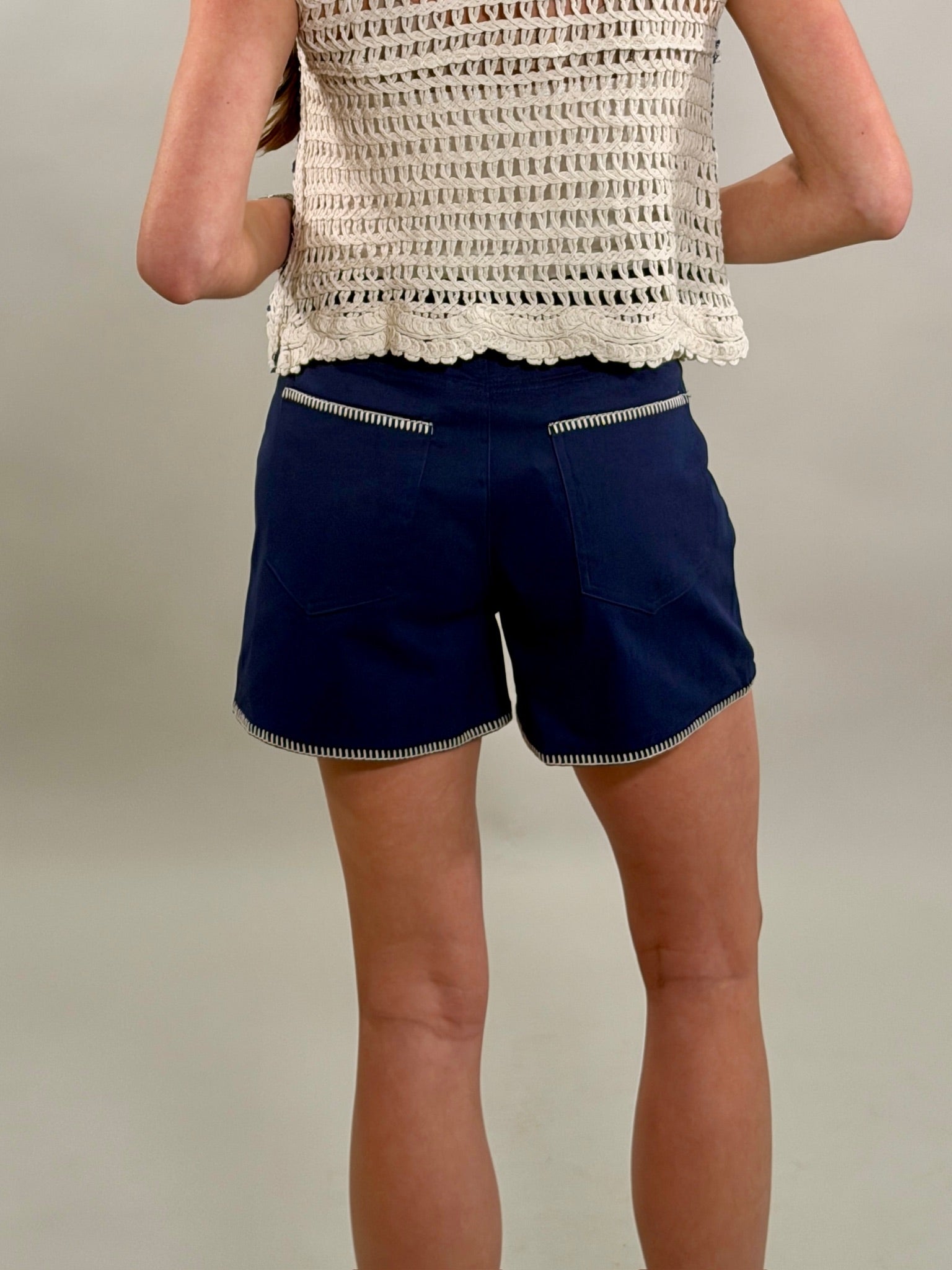 Rear view of a close-up of navy blue shorts featuring unique white contrast stitching on the pocket trim and hem.