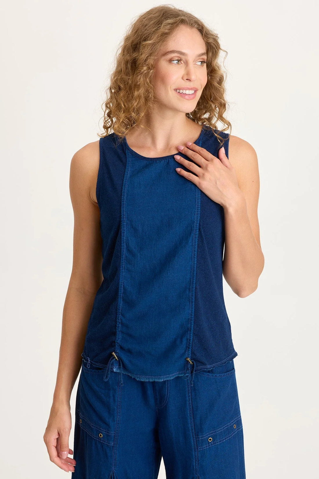 Front view of a woman with curly blonde hair wearing a dark indigo mixed-media tank top featuring adjustable front cinch cords and a raw-edge hem.