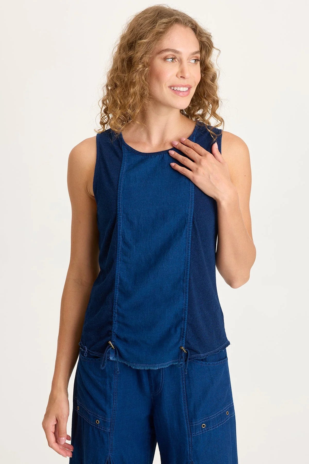 Front view of a woman with curly blonde hair wearing a dark indigo mixed-media tank top featuring adjustable front cinch cords and a raw-edge hem.