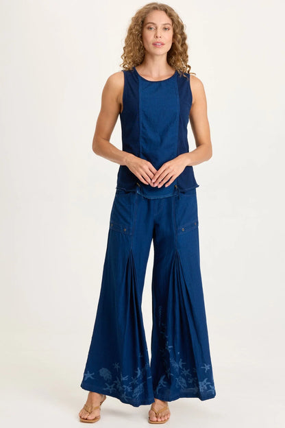 Full body view of a woman with curly blonde hair wearing a dark indigo mixed-media tank top featuring adjustable front cinch cords and a raw-edge hem.
