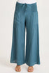 Front view of a woman wearing flowing teal-blue wide-leg linen pants with unique smocked side waist panels and deep front pockets.