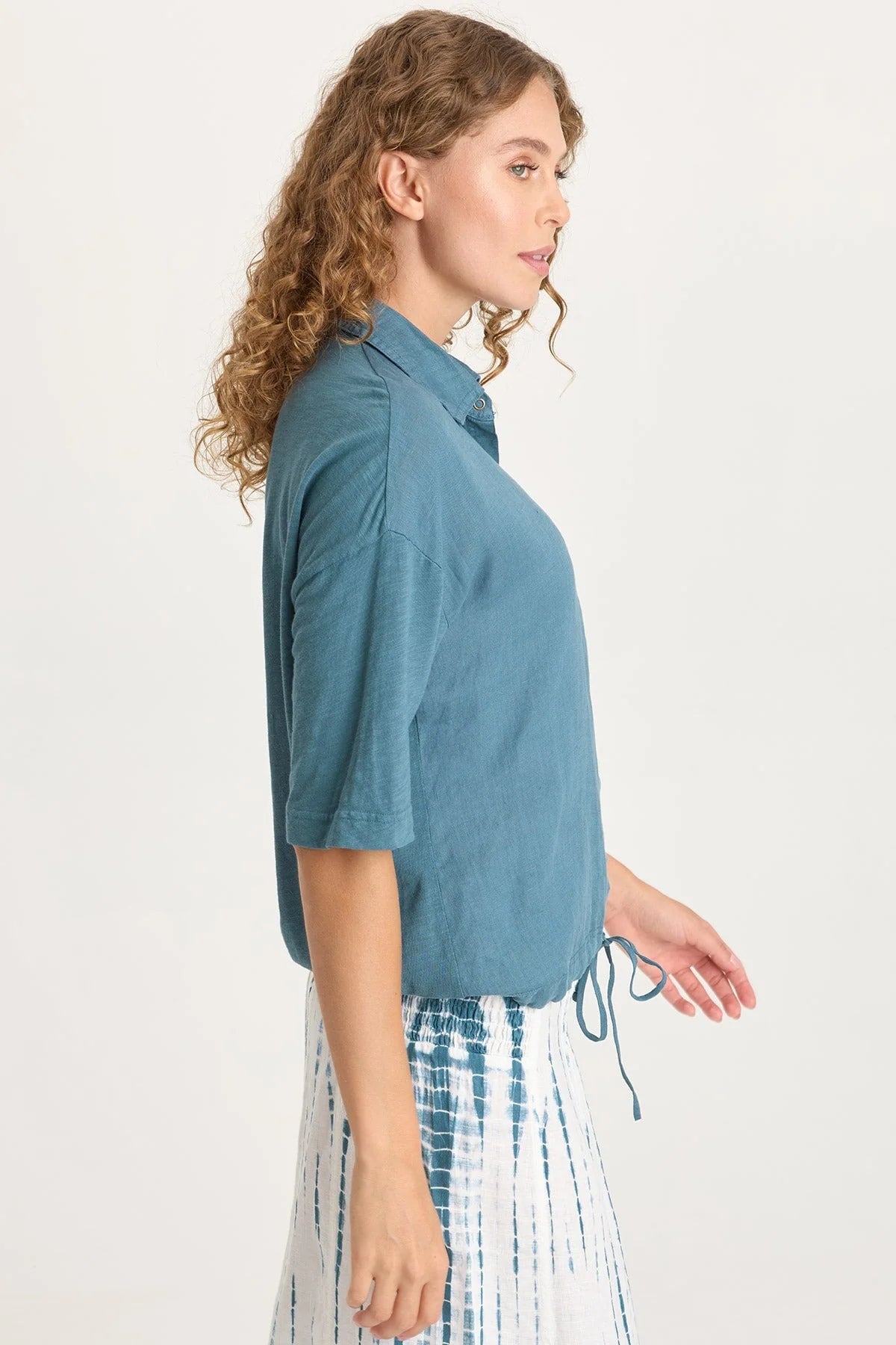 Side view of a woman wearing a blue shirt and plaid skirt on a white background