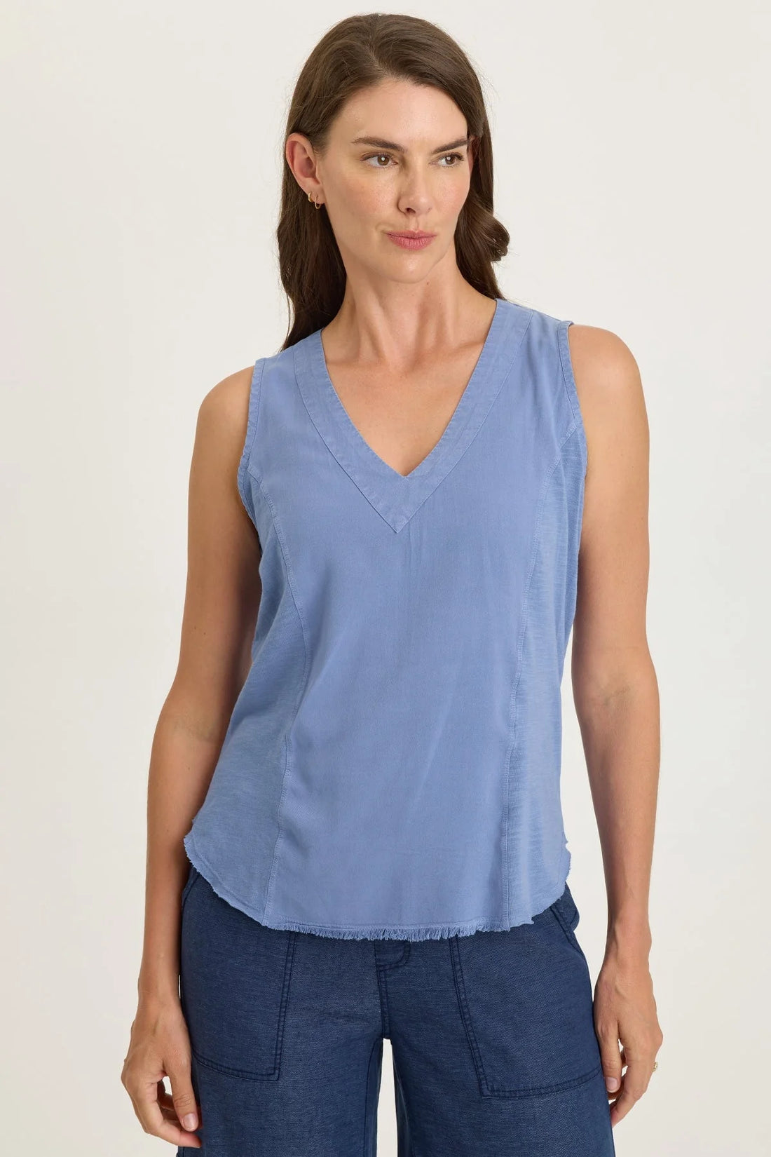 Woman wearing a light blue mixed-media sleeveless v-neck top with a frayed hem paired with navy blue pants.