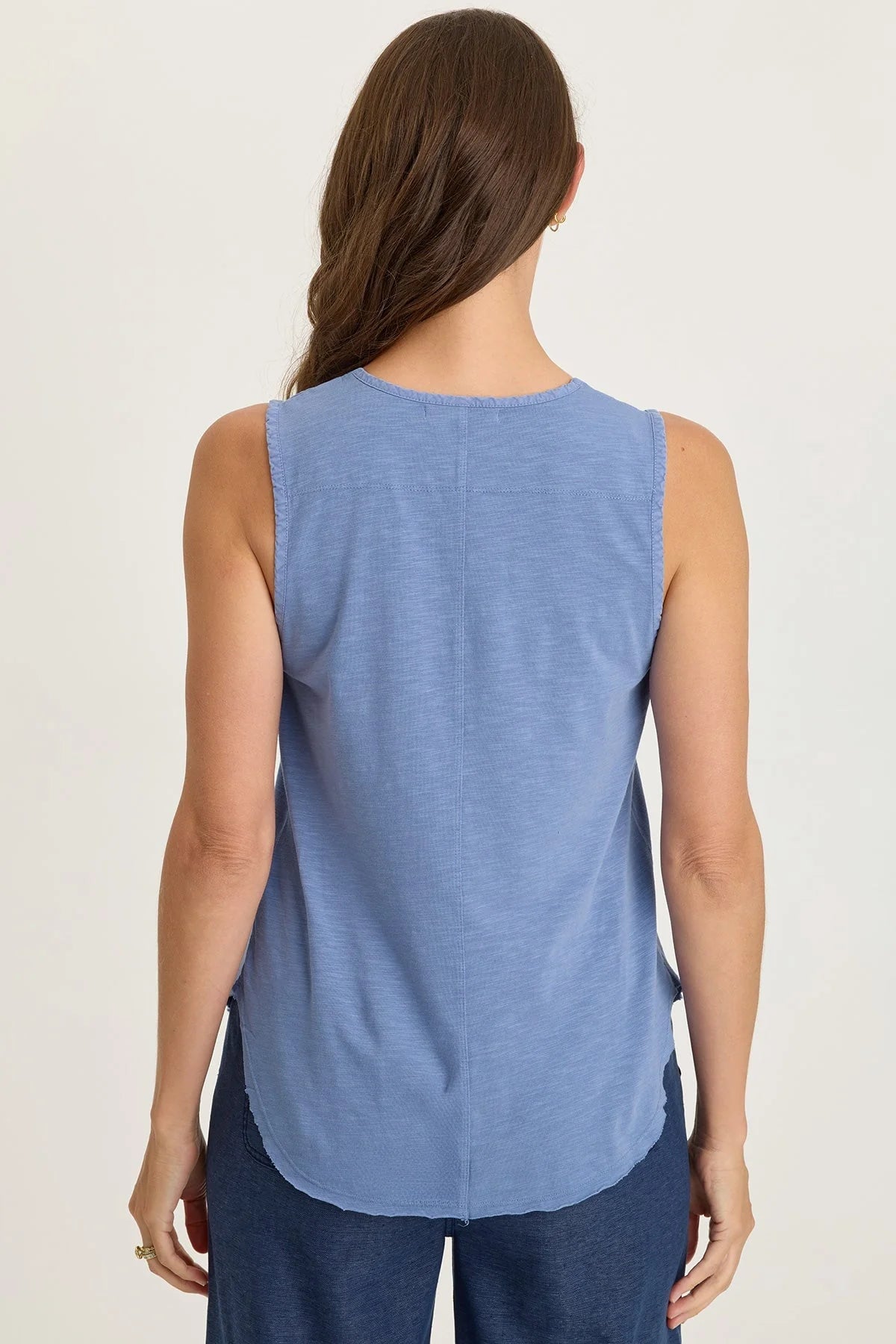 Rear view of a woman wearing a light blue mixed-media sleeveless v-neck top with a frayed hem paired with navy blue pants.