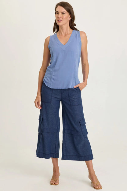 Full body view of a woman wearing a light blue mixed-media sleeveless v-neck top with a frayed hem paired with navy blue pants.