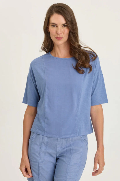 Front view of a woman with long brown hair wearing a light blue mixed-media short-sleeve top with matching blue pants.