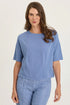 Front view of a woman with long brown hair wearing a light blue mixed-media short-sleeve top with matching blue pants.
