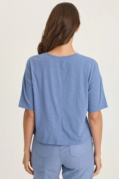 Rear view of a woman with long brown hair wearing a light blue mixed-media short-sleeve top with matching blue pants.