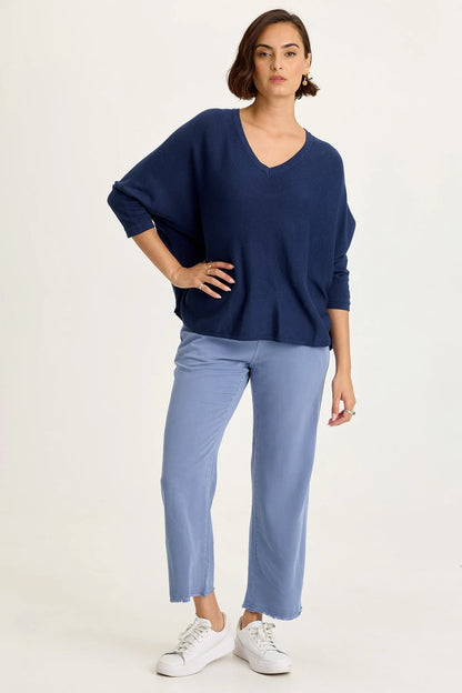 Full body view of a woman wearing light blue wide-leg twill pants with front pockets and a raw-edge frayed hem, paired with white sneakers.