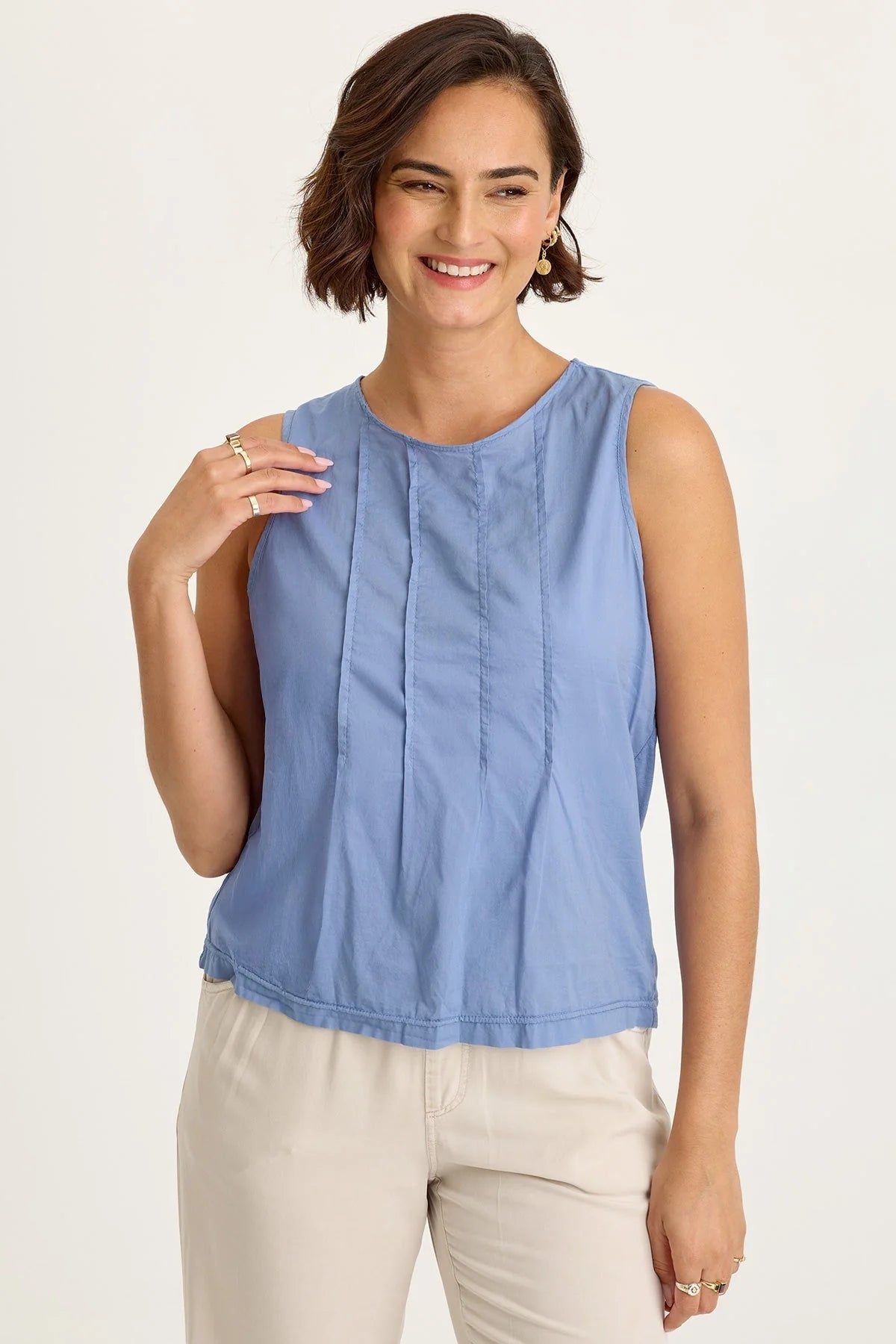 Woman wearing a blue sleeveless top and beige pants on a white background