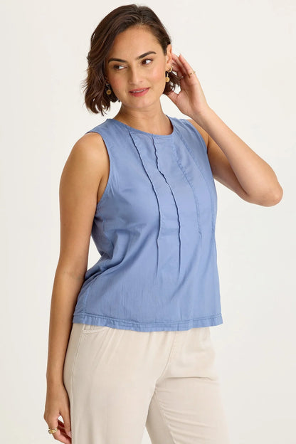 Side view of a woman wearing a light blue sleeveless top and beige pants on a plain background