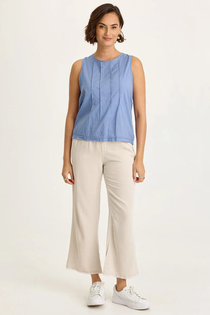 Full body view of a woman wearing a blue sleeveless top and beige pants on a white background