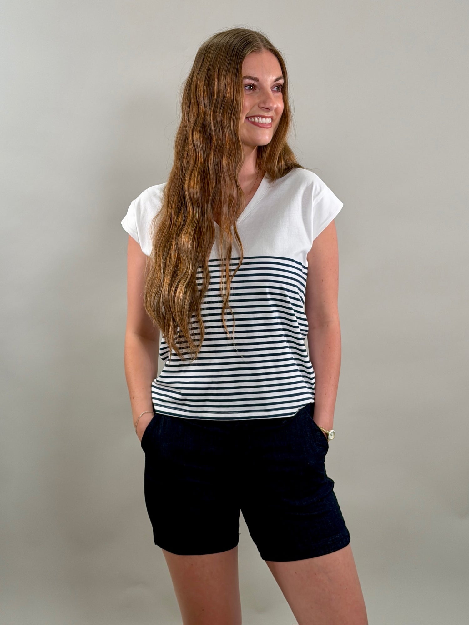 Smiling woman wearing a white t-shirt with navy stripes and navy shorts on a plain background.
