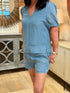 Close-up of a woman wearing light blue 100% lyocell shorts featuring lined floral eyelet cutouts on the front and practical side pockets.