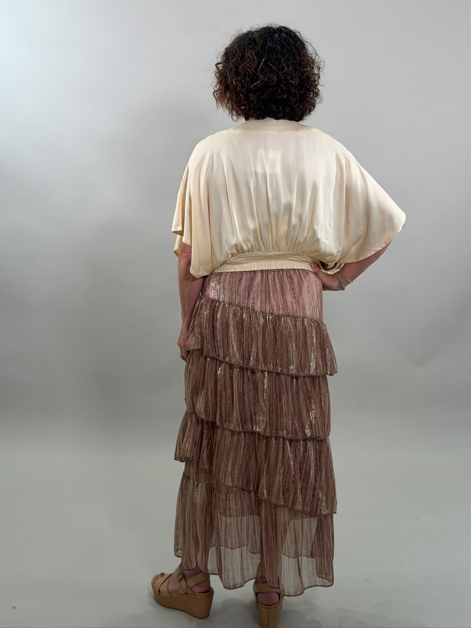 Rear view of a woman wearing a cream-colored bohemian blouse and a ruffled skirt with a smocked waist.