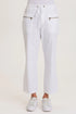 Front view of a woman wearing white structured seersucker flared pants with a drawstring waist and brass zipper pocket accents, paired with white sneakers.